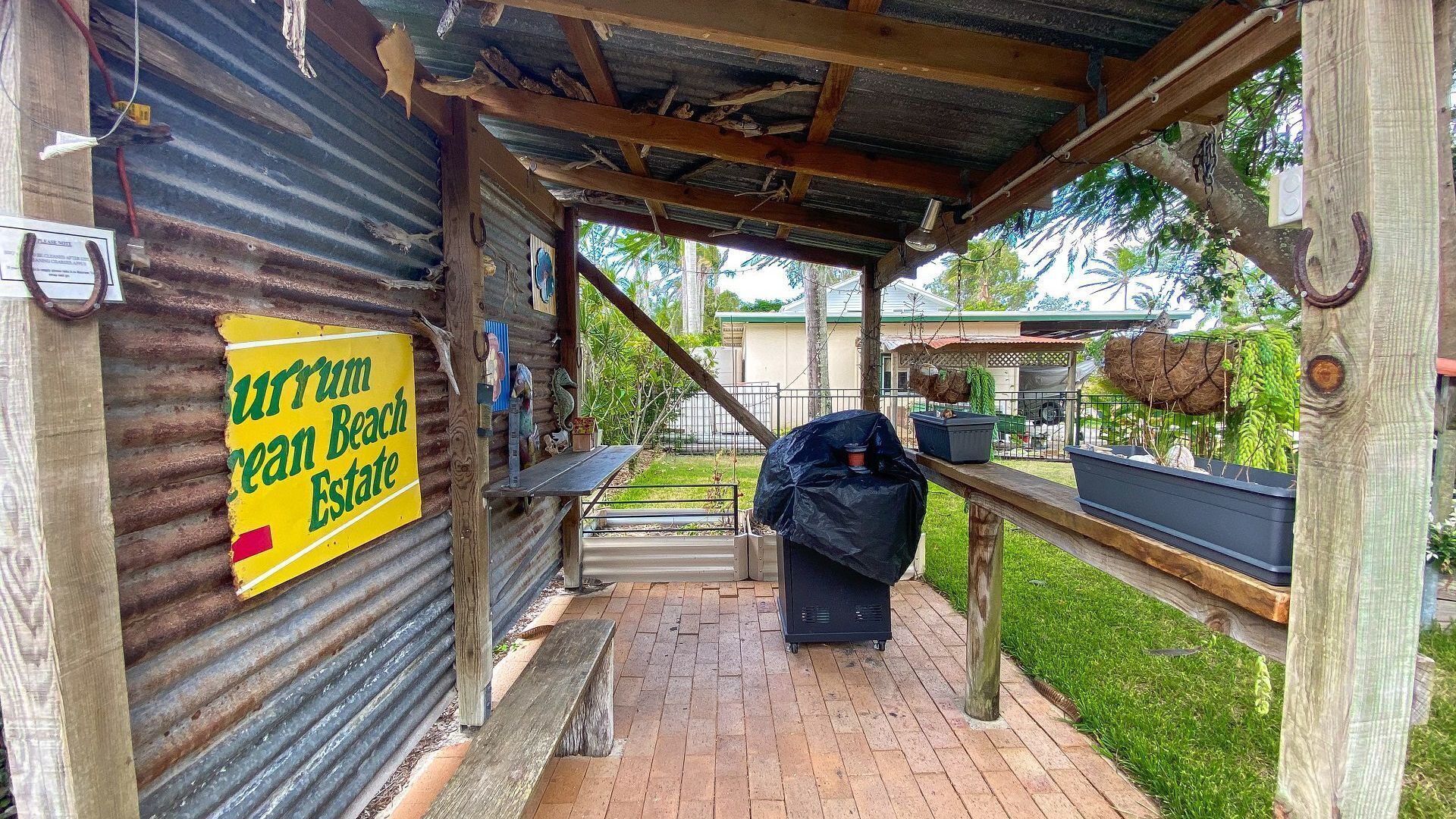 A rustic outdoor area with a wooden bench, a barbecue grill, and a sign for 'Curium Great Beach Estate'.