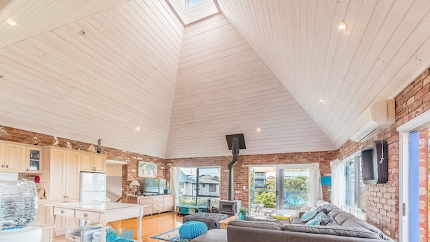A spacious living area with a high ceiling, a kitchen with modern appliances, and large windows offering views of the outside. - Mills Court, Quirky seaside house at Smiths Beach, bring the surf boards! (Smiths Beach)