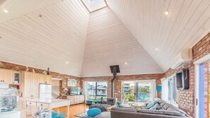A spacious living area with a high ceiling, a kitchen with modern appliances, and large windows offering views of the outside.