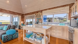 A spacious kitchen with a large island, a dining area with a sofa and cushions, and a view of the outdoors. - Mills Court, Quirky seaside house at Smiths Beach, bring the surf boards! (Smiths Beach)