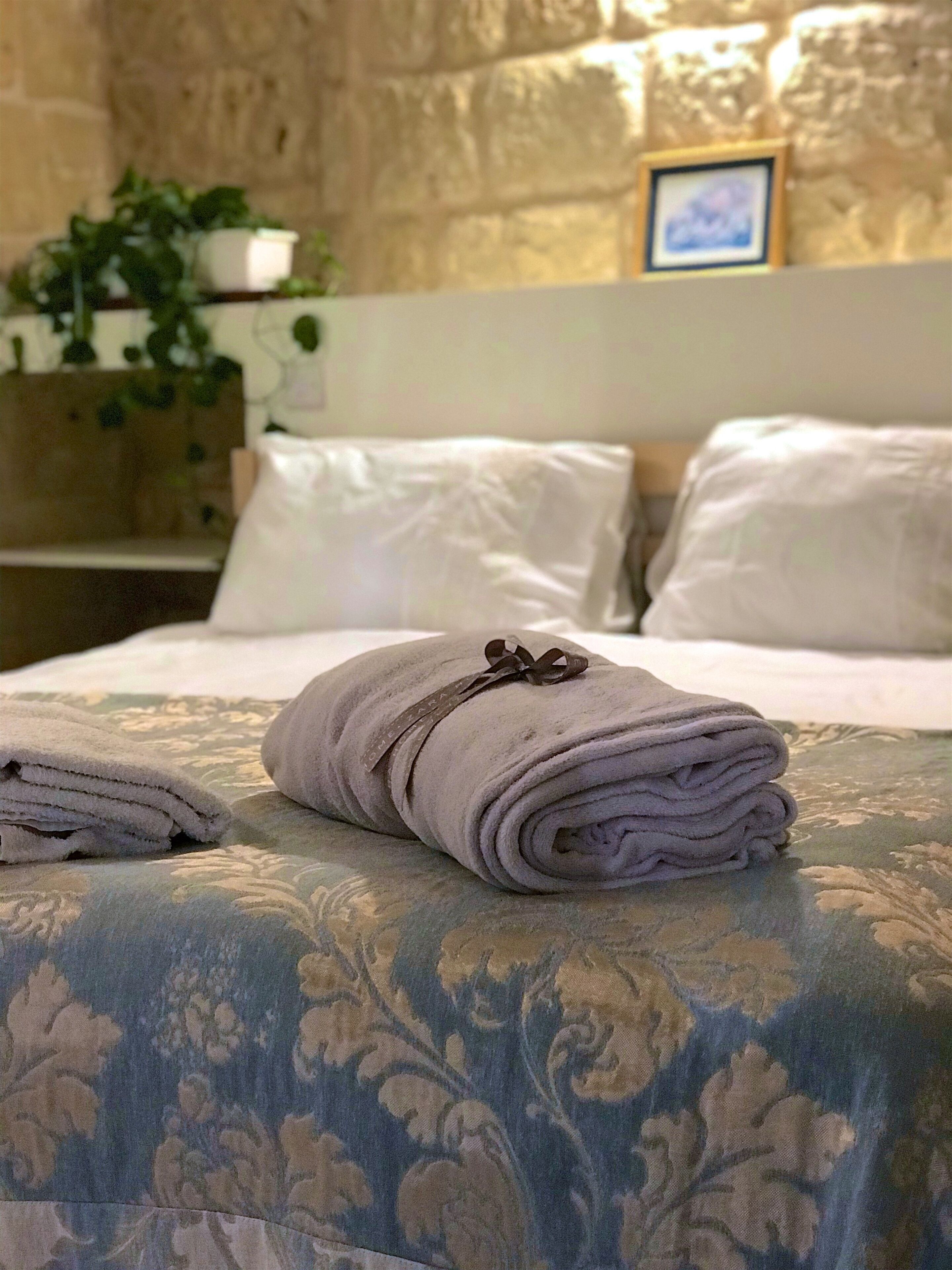 Een net opgemaakt bed met een opgerolde handdoek en een kussen op een beddegoed met een patroon.