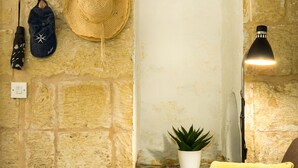 Una pared de piedra con un reloj, un sombrero, una lámpara y una planta.