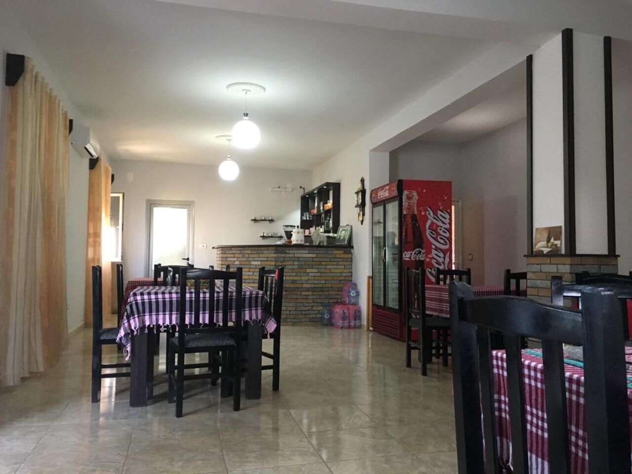 A dining area with a brick wall, a Coca-Cola refrigerator, and a kitchen in the background.