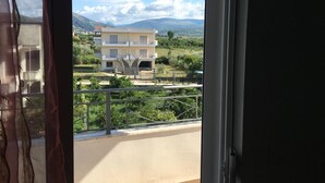 En balkon med udsigt til en bygning og et bjerrelandskab.