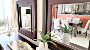 Een moderne hotelkamer met een grote spiegel, een houten bijzettafeltje met decoratieve objecten, en uitzicht op de eetruimte.