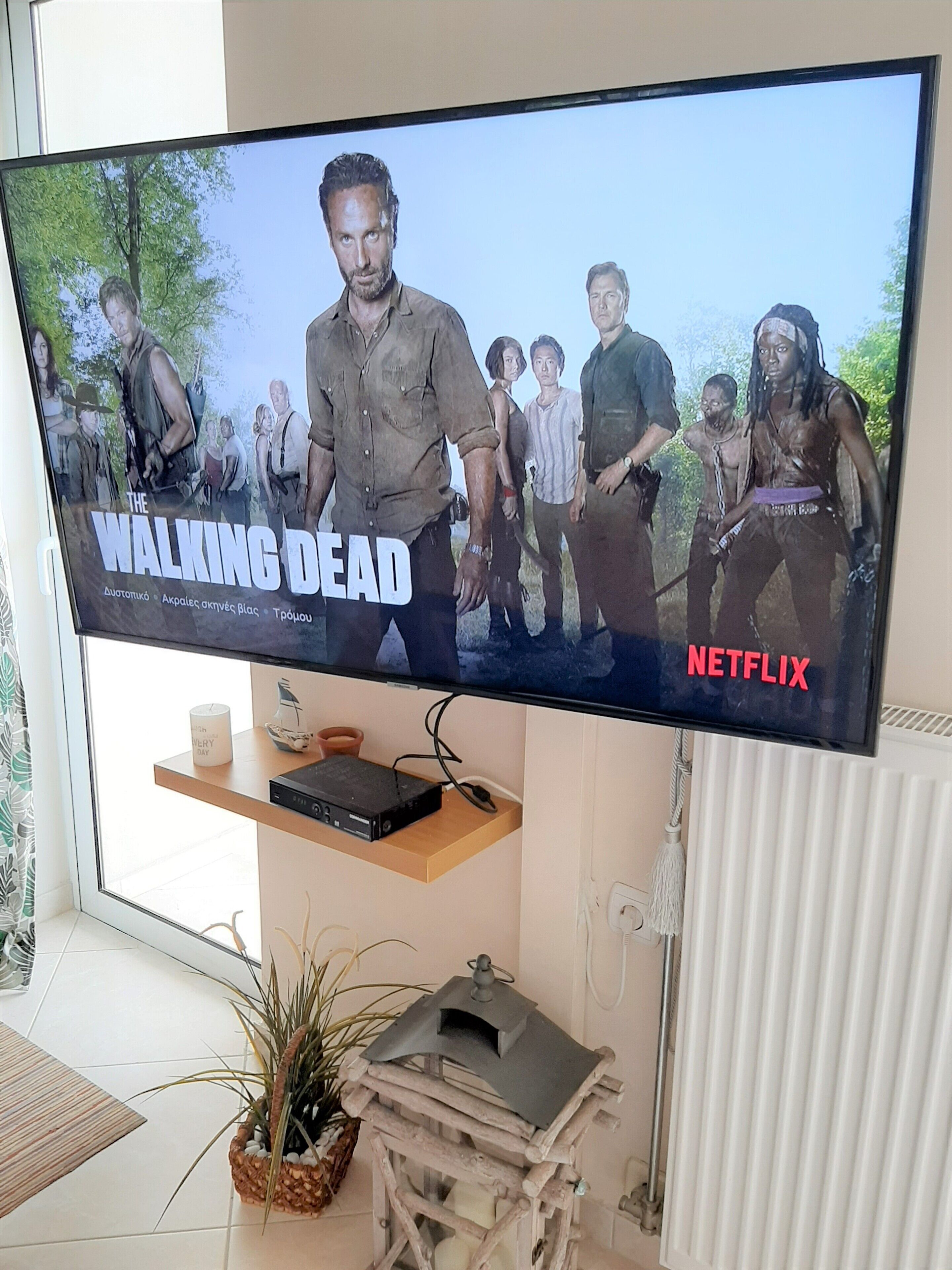 Ein Flachbildfernseher zeigt 'The Walking Dead' auf Netflix, darunter ein Regal mit einem DVD-Player und Dekorationsobjekten.