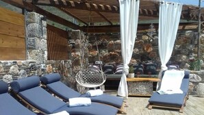 Een zonnig terras met houten ligstoelen en een muur van steen op de achtergrond.