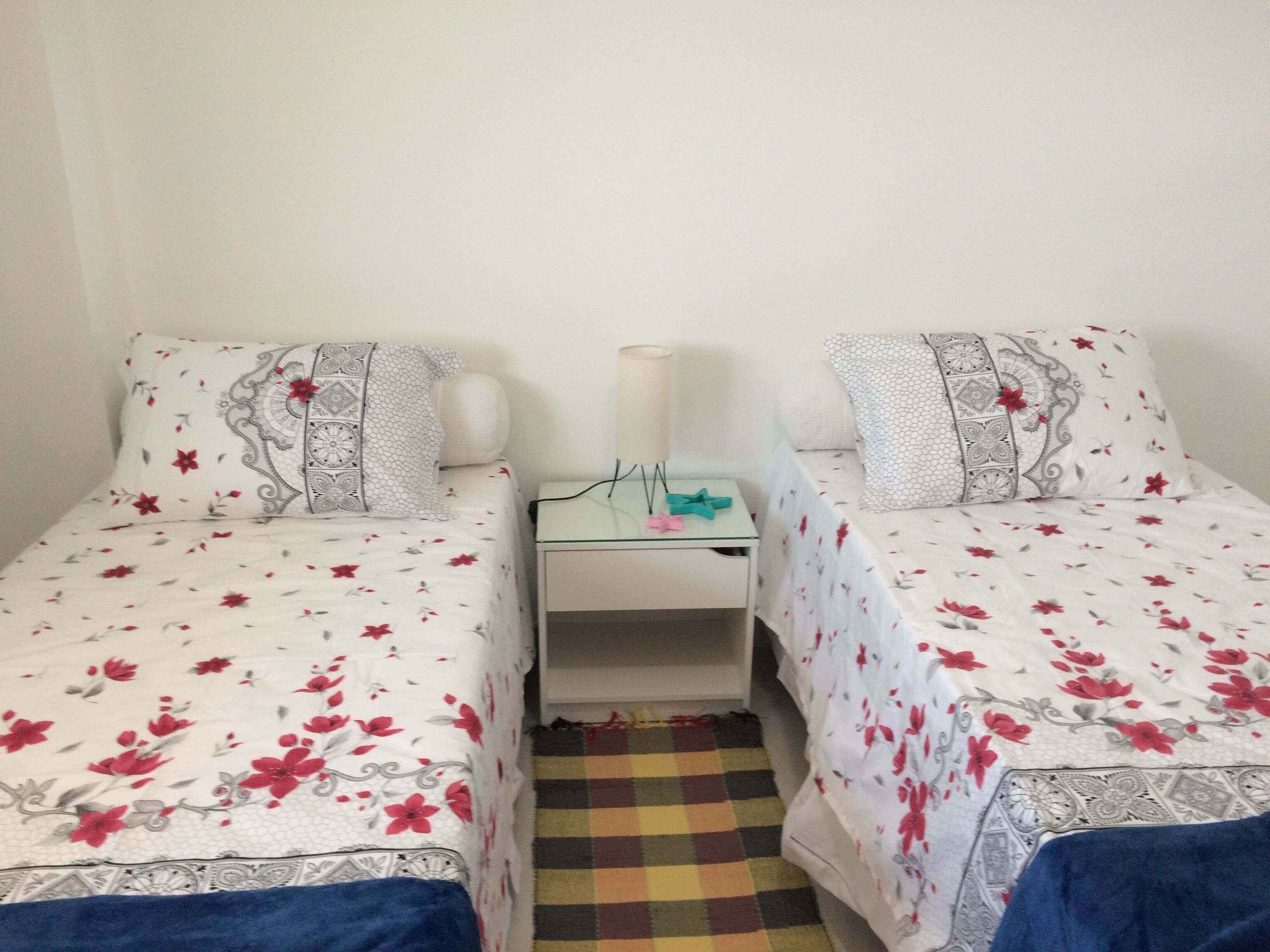 Camera doppia con due letti singoli, un comodino, una lampada e un tappeto a scacchi.