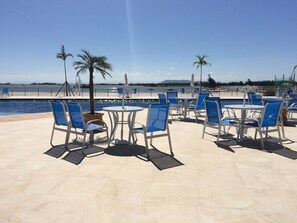 A poolside area with blue chairs and tables, palm trees, and a view of the water.