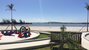 Un parque infantil con toboganes y columpios de colores, una banca y una palmera.