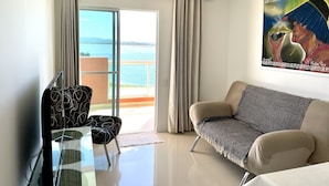 Una sala de estar moderna con una mesa de vidrio, un sofá estampado y vista al mar a través de amplios ventanales.