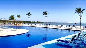 Una piscina con sillas de descanso y palmeras, con vista despejada al mar.