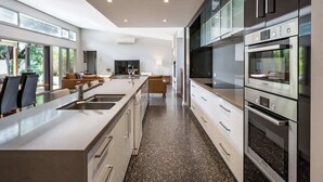 A modern kitchen with a central island, built-in appliances, and a view of the outdoors. - Mimosa—Stylish Beachside Retreat in Dunsborough (Dunsborough)
