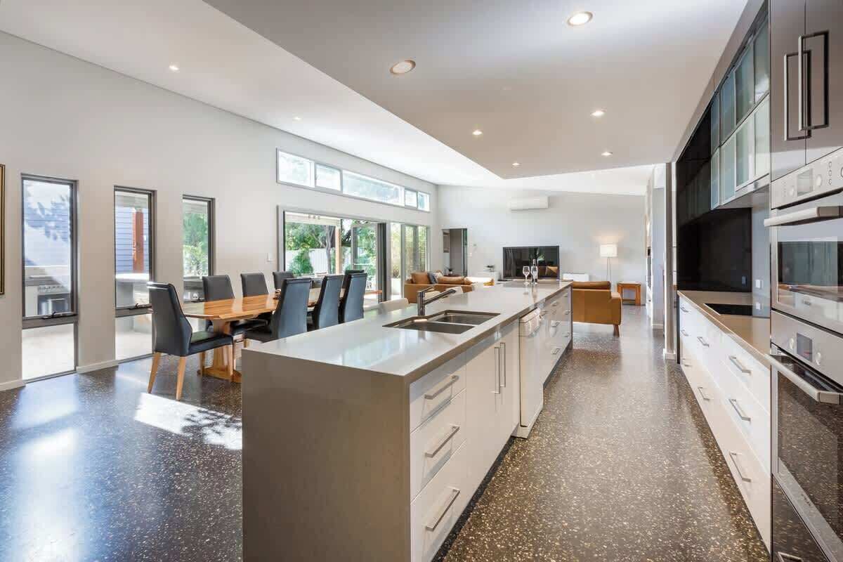 A modern kitchen with a central island, a dining area with chairs, and a large window.