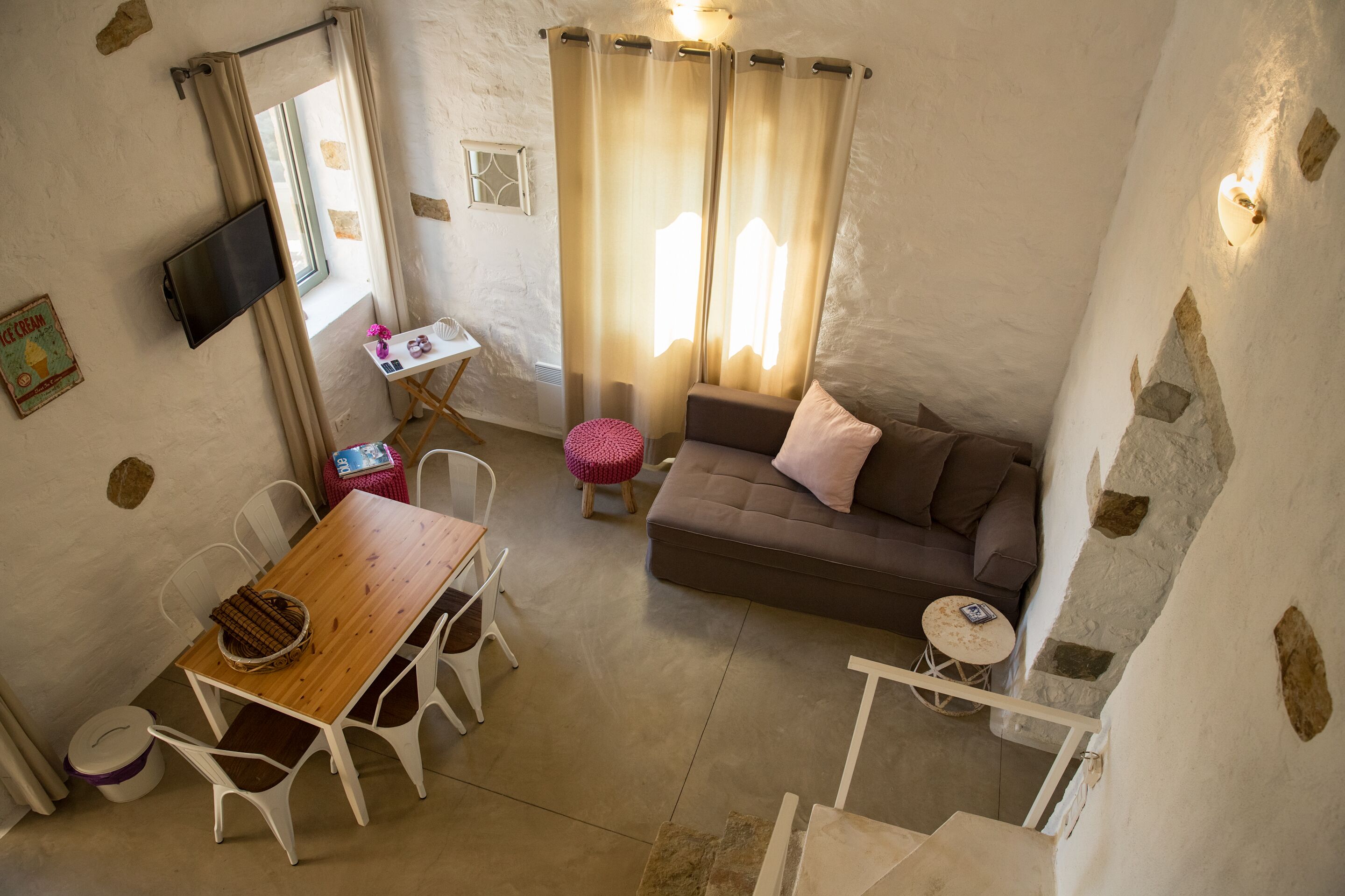 A cozy living room with a wooden dining table, white chairs, a brown sofa, and a small round table with a lamp.