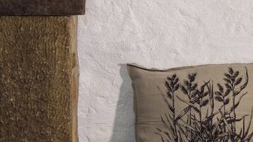 A rustic room with a stone shelf holding two pomegranates, a textured wall, a woven basket, and a cushion with a plant design.