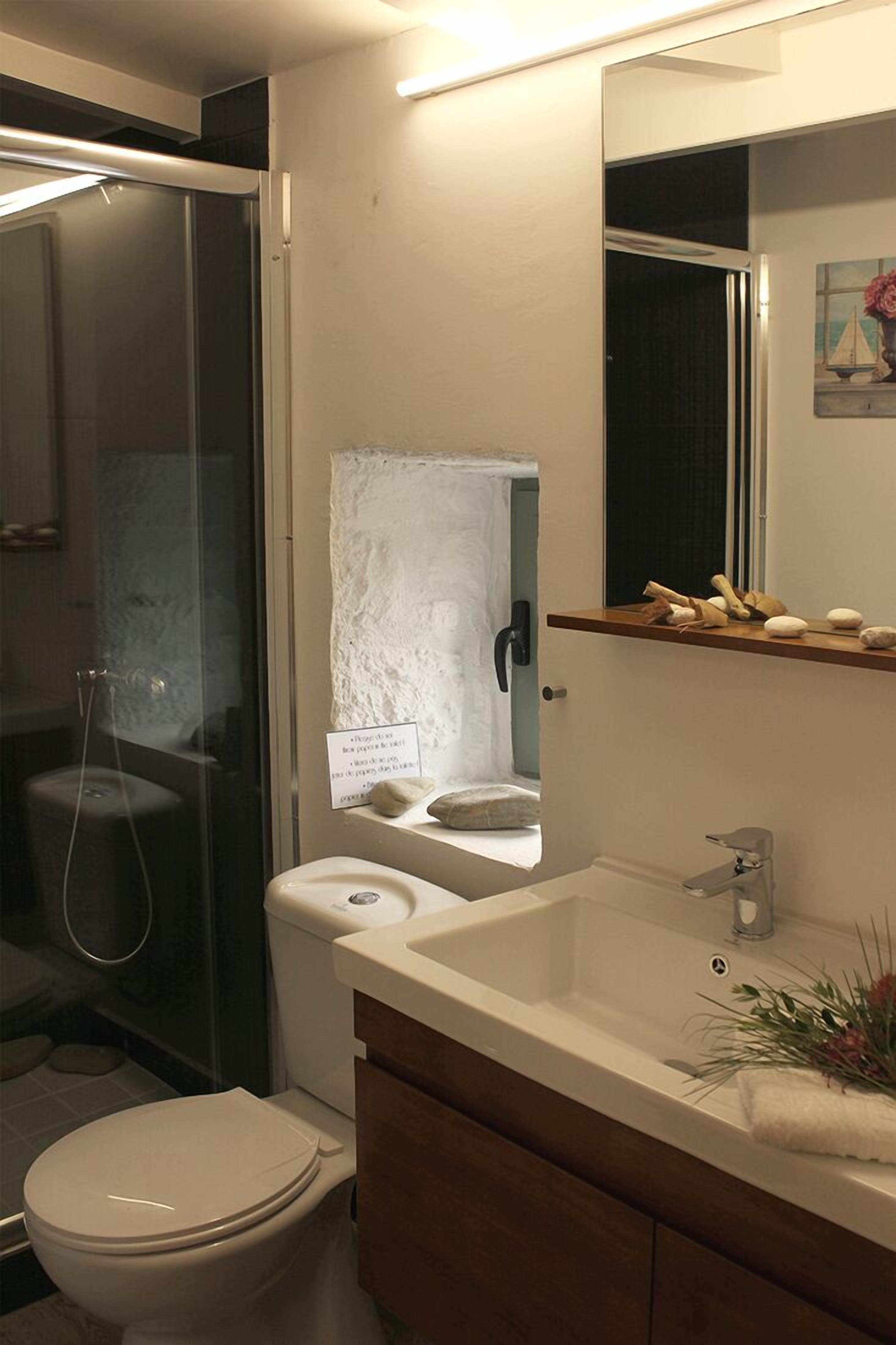 A modern bathroom with a glass shower enclosure, a toilet, a sink with a mirror, and a small shelf with toiletries.
