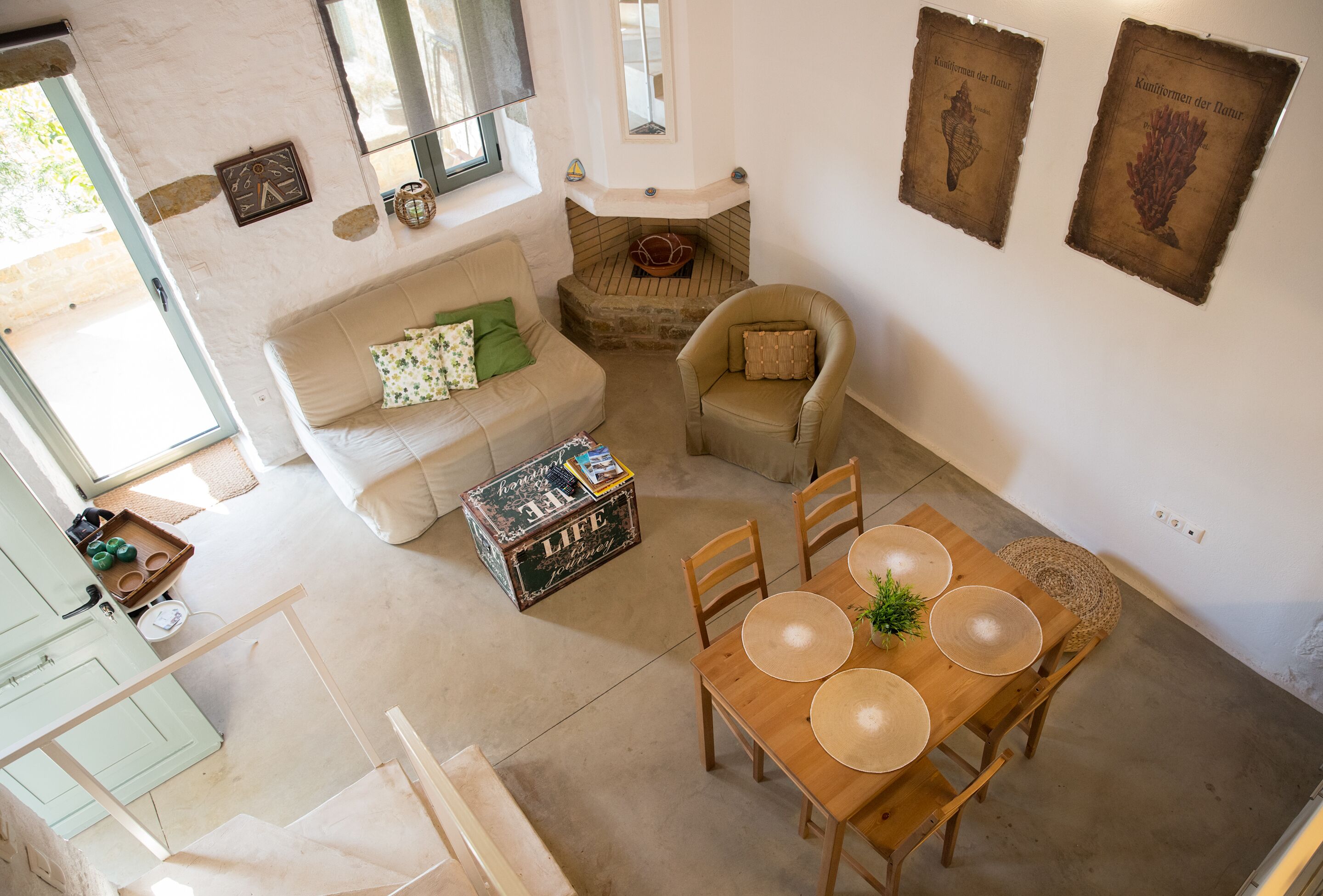 Un accogliente soggiorno con un divano, un tavolo da pranzo in legno con sottopiatti, una poltrona e una scatola decorativa con la scritta 'LIFE is a journey'.