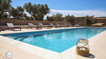 Una piscina con sillones de descanso y un tarro de vidrio en el borde.