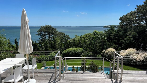 A wooden deck with outdoor furniture, a pool, and a view of the sea.