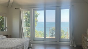 A spacious bedroom with a large window offering a view of the sea.