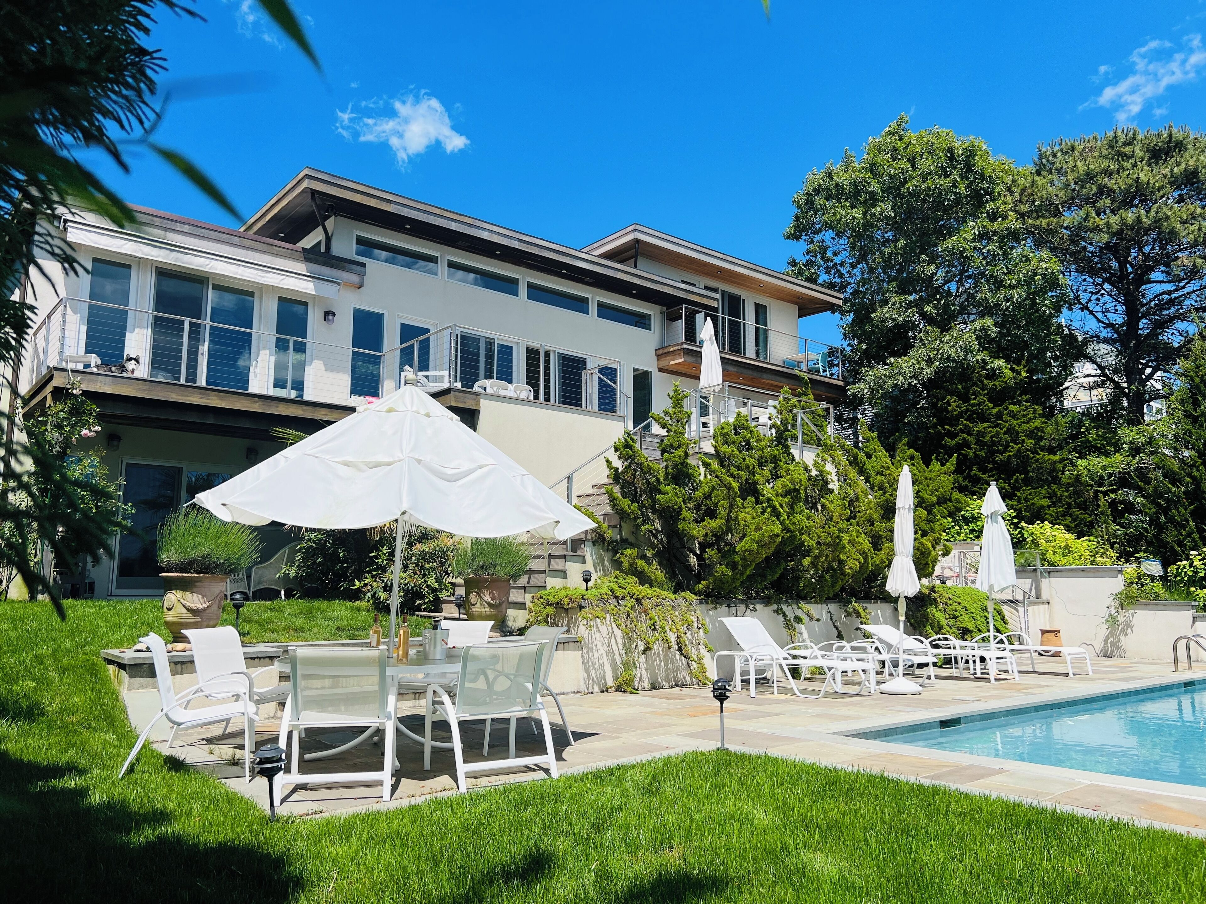 A modern two-story house with a swimming pool, outdoor seating, and lush greenery.