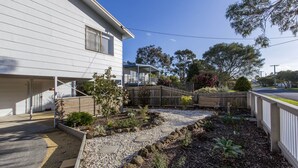 Een woonhuis met een overdekte patio, een tuin met verschillende planten en een klein vijvertje, en een houten omheining.