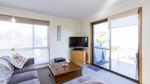 Een moderne woonkamer met een bank, een salontafel, een televisie op een houten kast en een schuifpui naar een buitenbalkon.