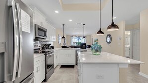 Una cocina moderna con electrodomésticos de acero inoxidable, armarios blancos, iluminación colgante y una isla grande.
