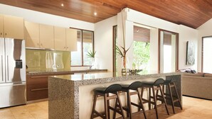 A modern kitchen with a granite island, bar stools, and a built-in refrigerator.