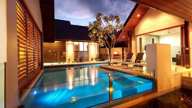 A modern outdoor pool area with a clear blue pool, lounge chairs, and a well-lit patio.