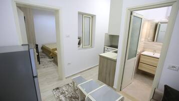 A compact hotel room with a kitchenette, a small dining table, a single bed, and a bathroom with a mirror and sink.