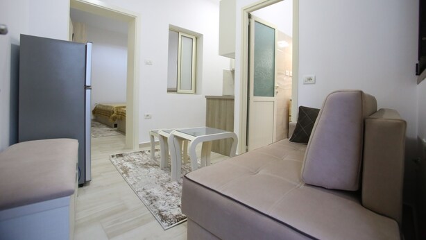 A compact living space with a sofa, a small table, a refrigerator, and a glass door leading to another room. - Idrizi Apartment (Berat)