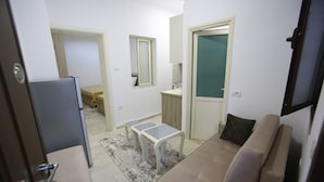 A compact living space with a sofa, a small table, and a kitchenette area. - Idrizi Apartment (Berat)