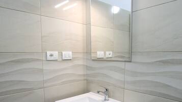 A modern bathroom with a white sink, wooden cabinet, and a wall-mounted mirror.