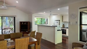 A modern kitchen with a central island, a dining area with wicker chairs, and a view of a pool through a screened door. - 8 Orania Court - Rainbow Shores. Privacy, Peace and Quiet (RAINBOW BEACH)