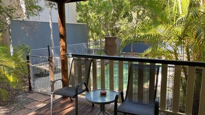 A deck with two chairs and a table, surrounded by a wooden railing, overlooking a pool and lush greenery. - 8 Orania Court - Rainbow Shores. Privacy, Peace and Quiet (RAINBOW BEACH)