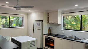 A modern kitchen with white cabinets, a built-in oven, a refrigerator, and a window with a view of greenery. - 8 Orania Court - Rainbow Shores. Privacy, Peace and Quiet (RAINBOW BEACH)