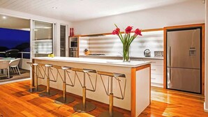 A modern kitchen with a central island, bar stools, a refrigerator, and a view of the outdoors.