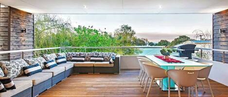 A modern outdoor patio with a wooden deck, a seating area with patterned cushions, and a dining table with chairs.
