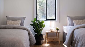 Une chambre avec deux lits, une fenêtre, une table de chevet avec une lampe et une plante en pot.