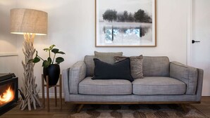 Un salon avec un canapé gris, un coussin noir, un plancher en bois, une cheminée, une lampe et un tableau encadré accroché au mur.