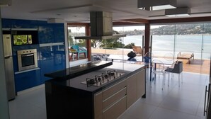 Una cocina moderna con una isla central, electrodomésticos integrados y grandes ventanales con vistas al mar.