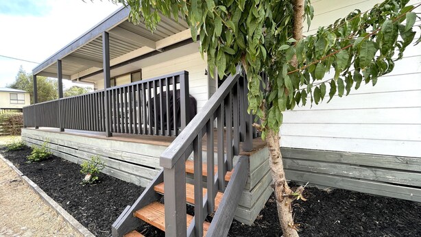 A covered porch with a wooden railing and steps leading to a white building. - Shelby s Lodge- lovely light filled home (Venus Bay)