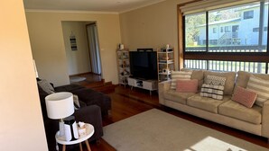 A living room with a sofa, TV, and shelves. - Shelby s Lodge- lovely light filled home (Venus Bay)