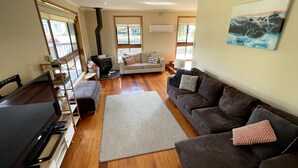A living room with a sofa, a coffee table, a fireplace, and a painting on the wall. - Shelby s Lodge- lovely light filled home (Venus Bay)