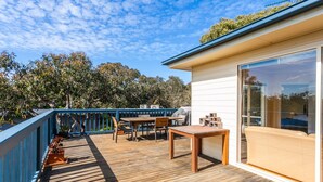 A wooden deck with a table and chairs, a barbecue grill, and a glass door leading to a covered area.