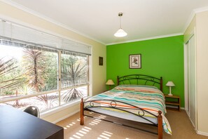 Een slaapkamer met een bed, een bureau, een raam met zonwering, een groene wand en een plafondlamp.