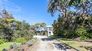 A two-story house with a covered porch and a gravel driveway leading to the entrance.
