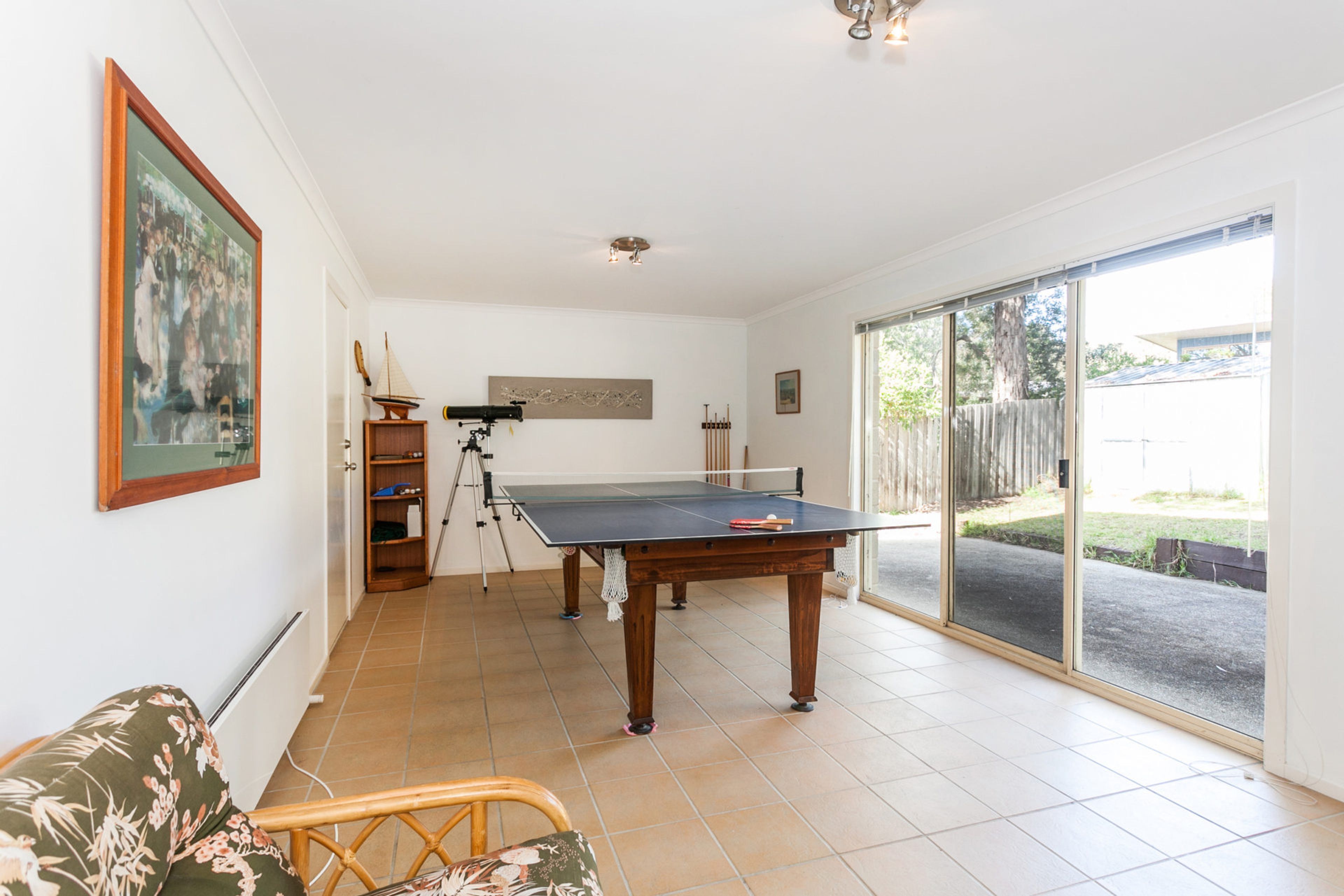 A room with a ping pong table, a telescope, and a framed picture on the wall.